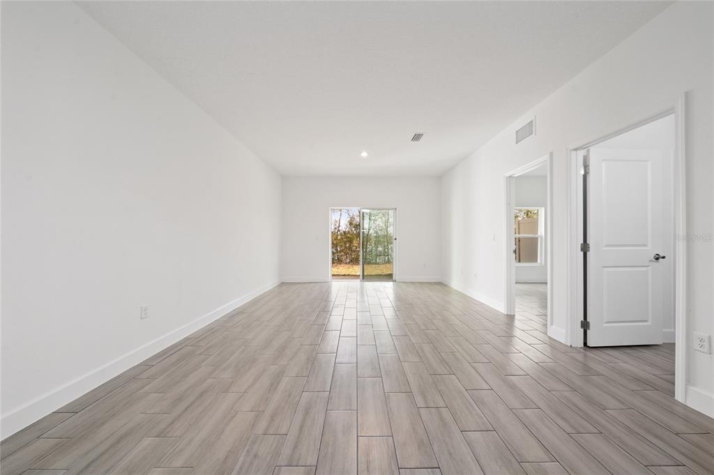 A bright, empty room features light wood-look tile flooring, white walls, and a sliding glass door — 462 LAKE SHORE PARKWAY, DAVENPORT, FL