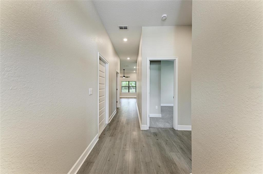 A hallway with light wood-look flooring leads toward a room with a window and fan — 9421 43RD COURT E, PARRISH, FL