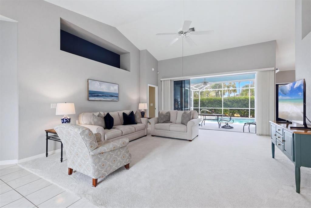 A living room features a vaulted ceiling, neutral carpet, and a sliding door to a pool — 1787 KILRUSS DRIVE, VENICE, FL
