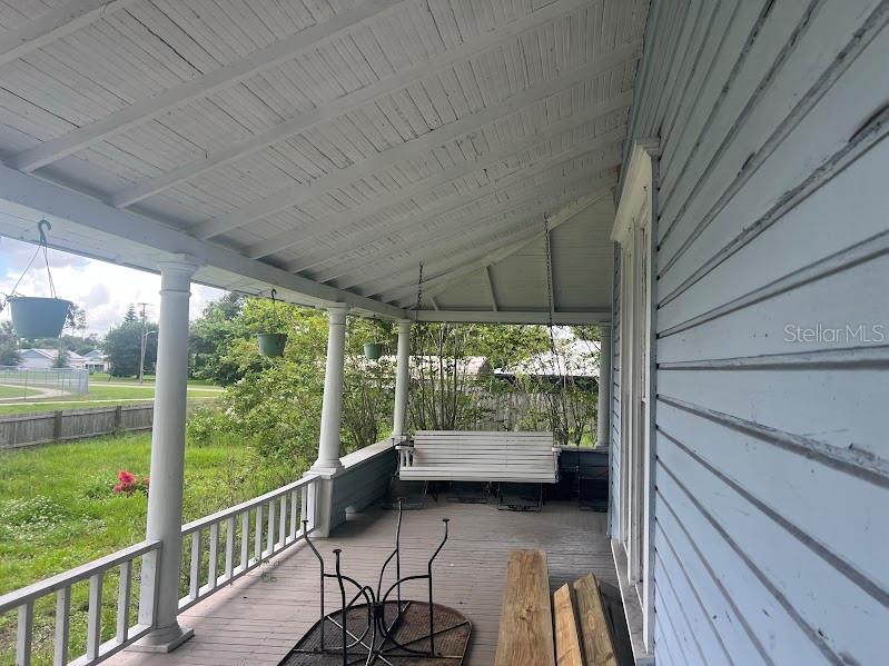 A covered wooden porch features white columns, a hanging bench, and a view of a yard — 523 N LEE AVENUE, ARCADIA, FL