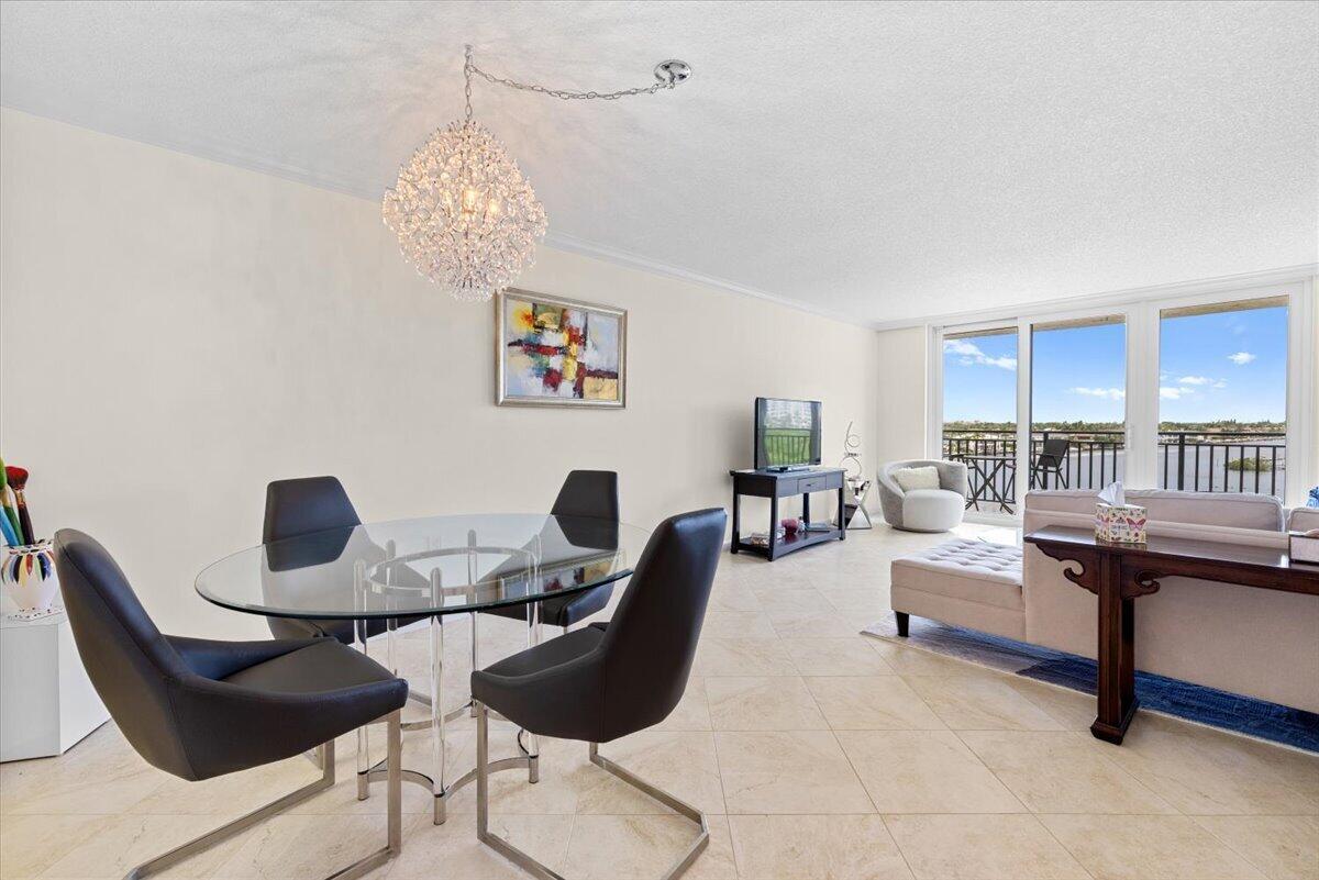 A dining area with a glass table and chandelier opens into a living room with balcony — 3912 S Ocean Boulevard # 603, Highland Beach FL 33487, HIGHLAND BEACH, FL