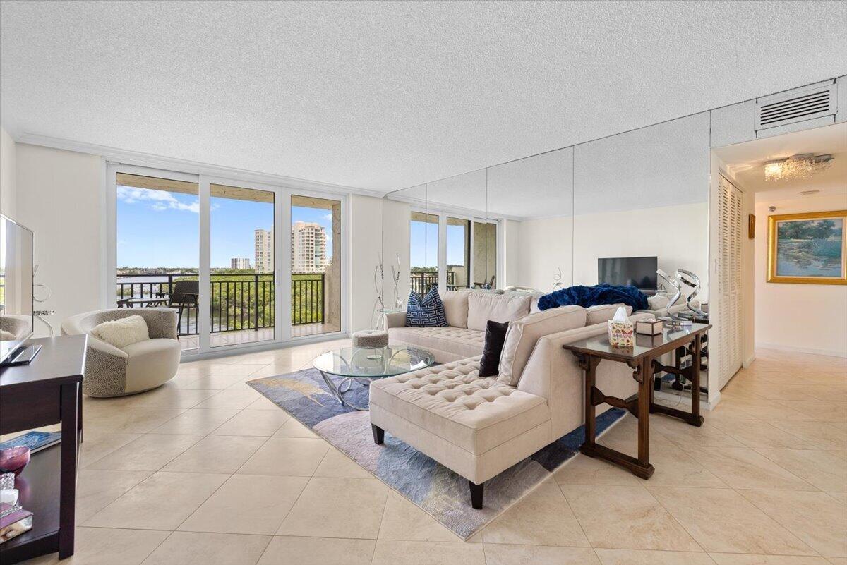 A living room with tile floors, a mirrored wall, and a balcony overlooking green trees — 3912 S Ocean Boulevard # 603, Highland Beach FL 33487, HIGHLAND BEACH, FL