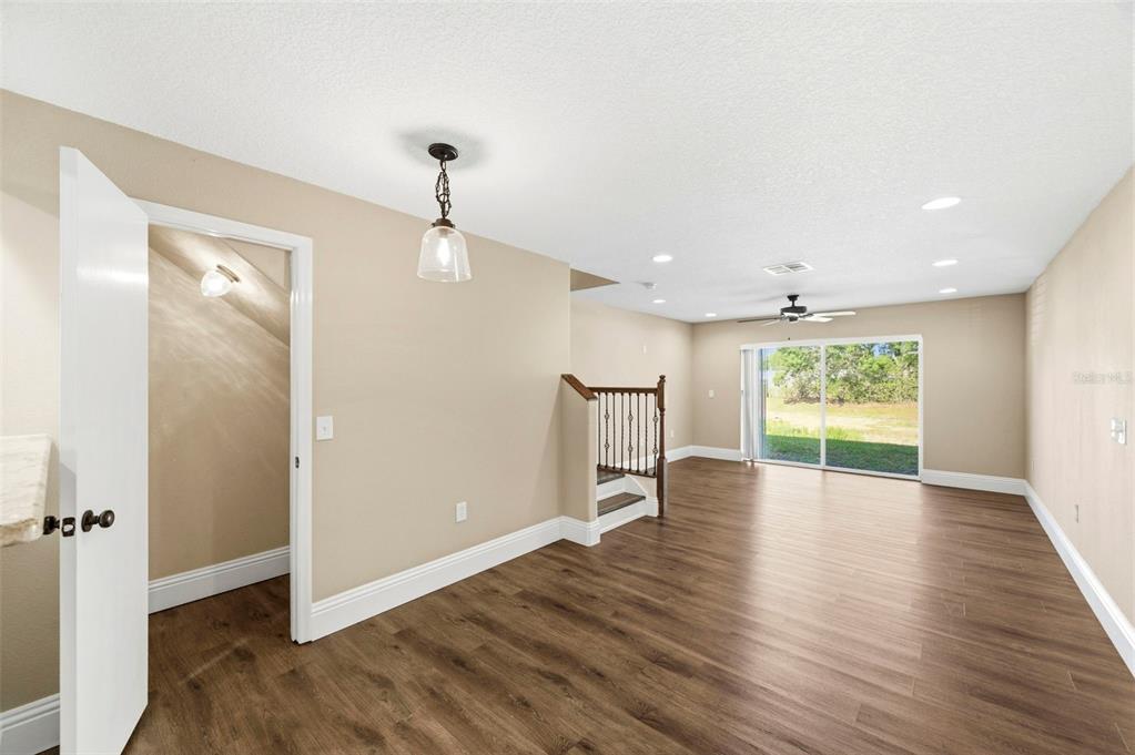 An empty room with wood-look flooring, a staircase, a pendant light, and sliding glass doors — 6811 DARTMOUTH HILL STREET, RIVERVIEW, FL
