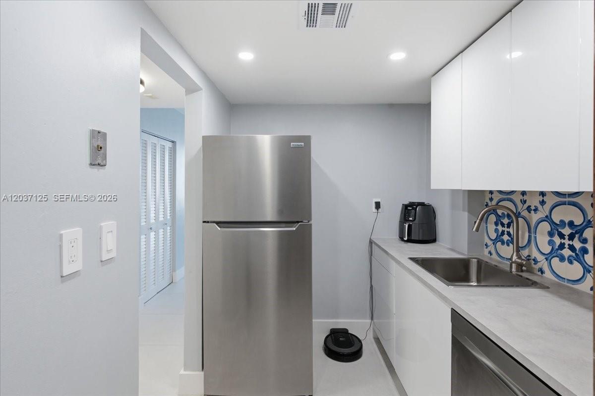 A kitchen features a stainless steel refrigerator, white cabinets, a sink, and patterned blue backsplash — 2899 Collins Ave # 1022, Miami Beach FL 33140, MIAMI BEACH, FL
