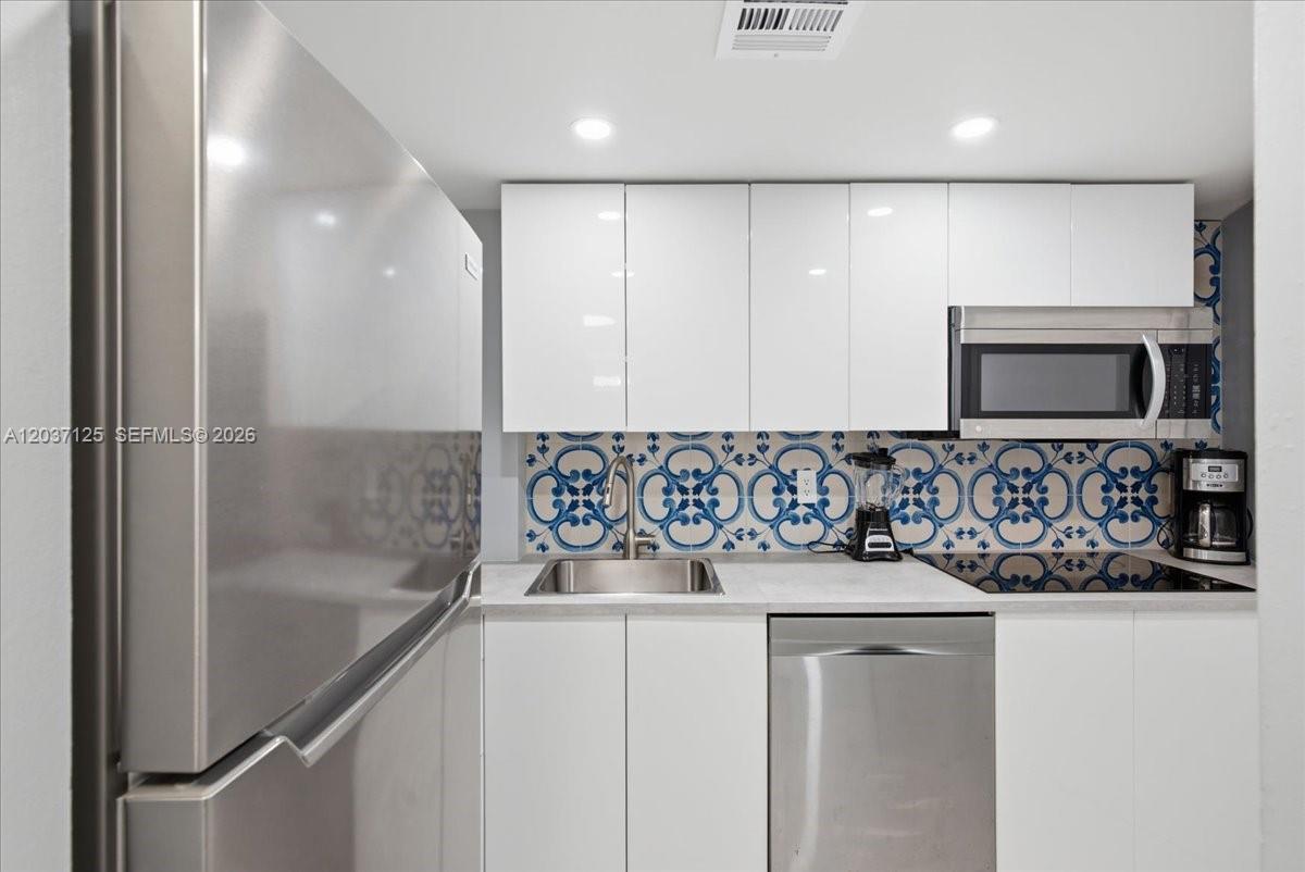 A modern kitchen features white cabinets, stainless steel appliances, and a blue patterned tile backsplash — 2899 Collins Ave # 1022, Miami Beach FL 33140, MIAMI BEACH, FL