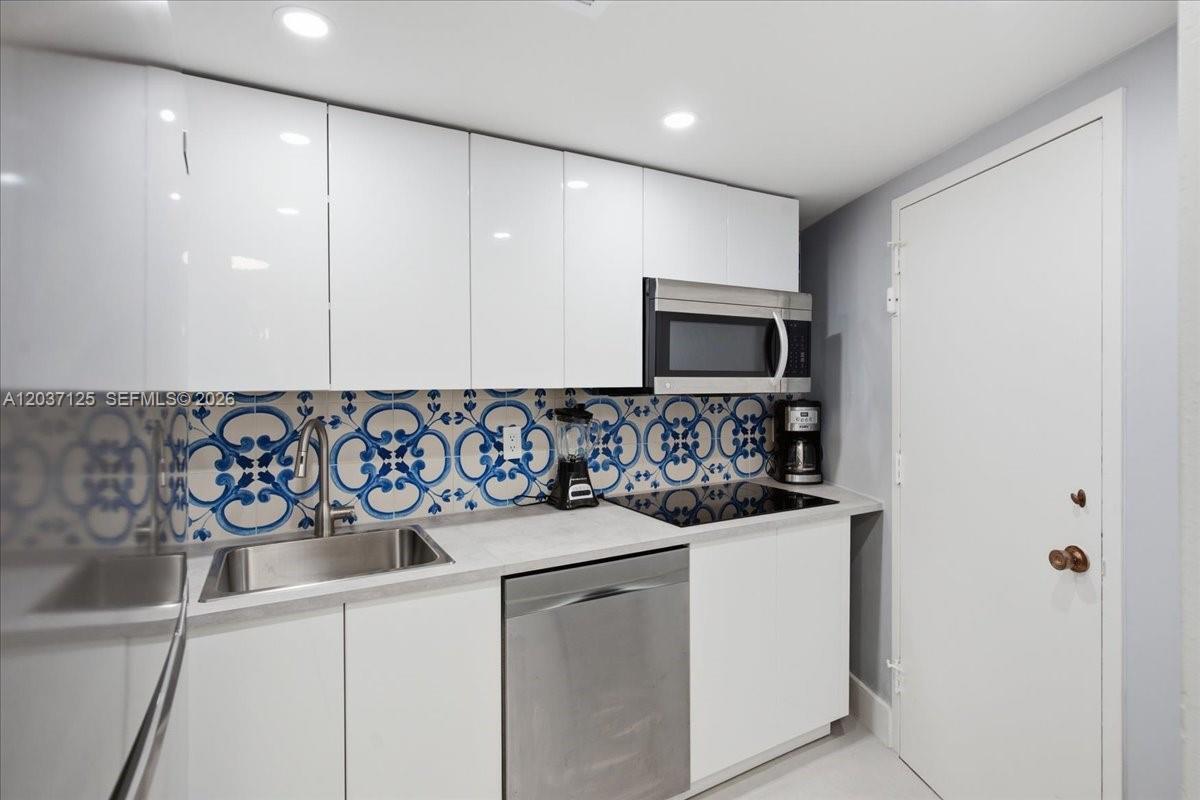 A small kitchen features white cabinets, a patterned blue backsplash, and stainless steel appliances — 2899 Collins Ave # 1022, Miami Beach FL 33140, MIAMI BEACH, FL
