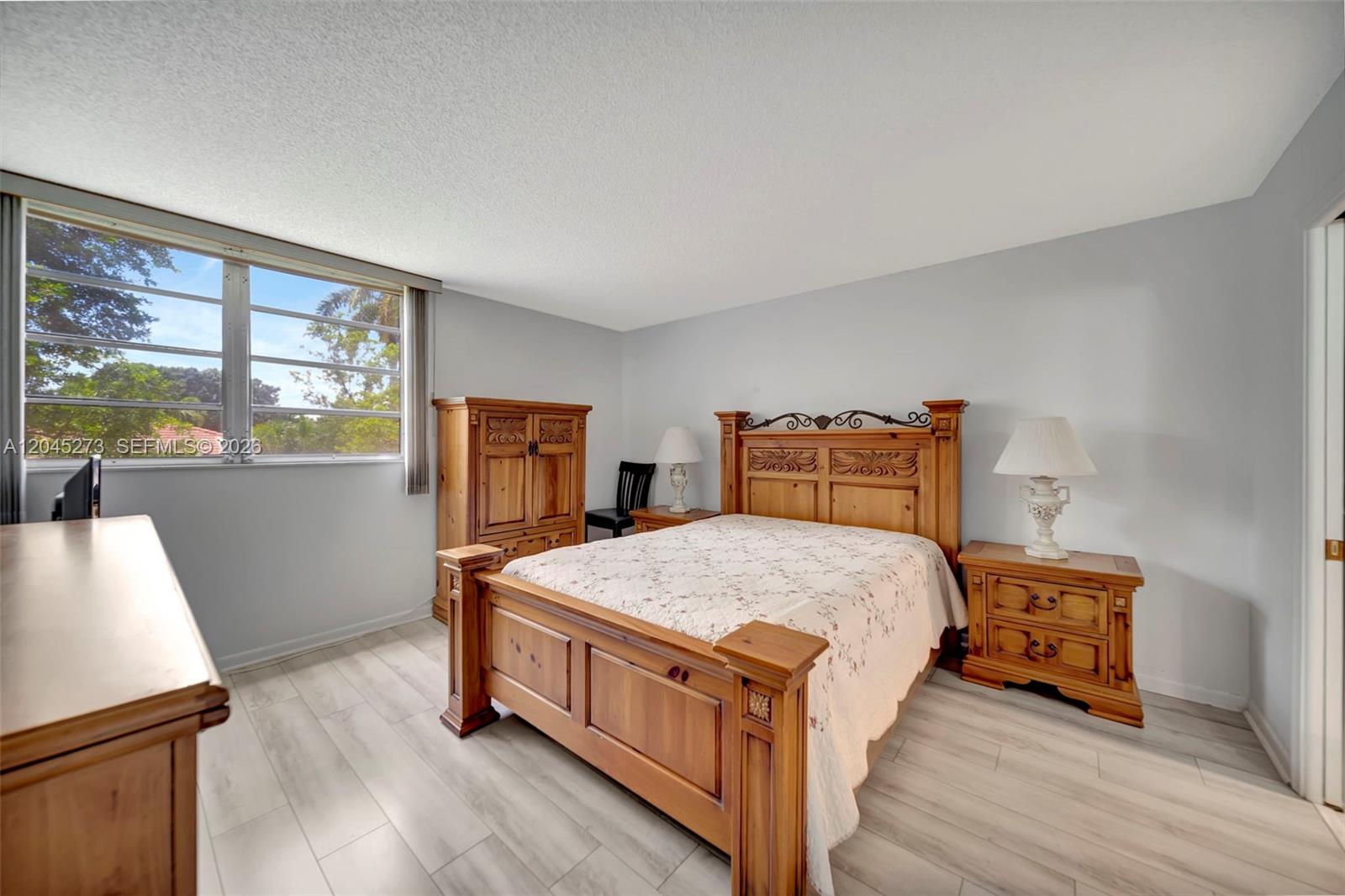 A bedroom features a wooden bed frame, matching furniture, and light-colored wood-look flooring — 2571 Aragon Blvd # 220, Sunrise FL 33322, SUNRISE, FL