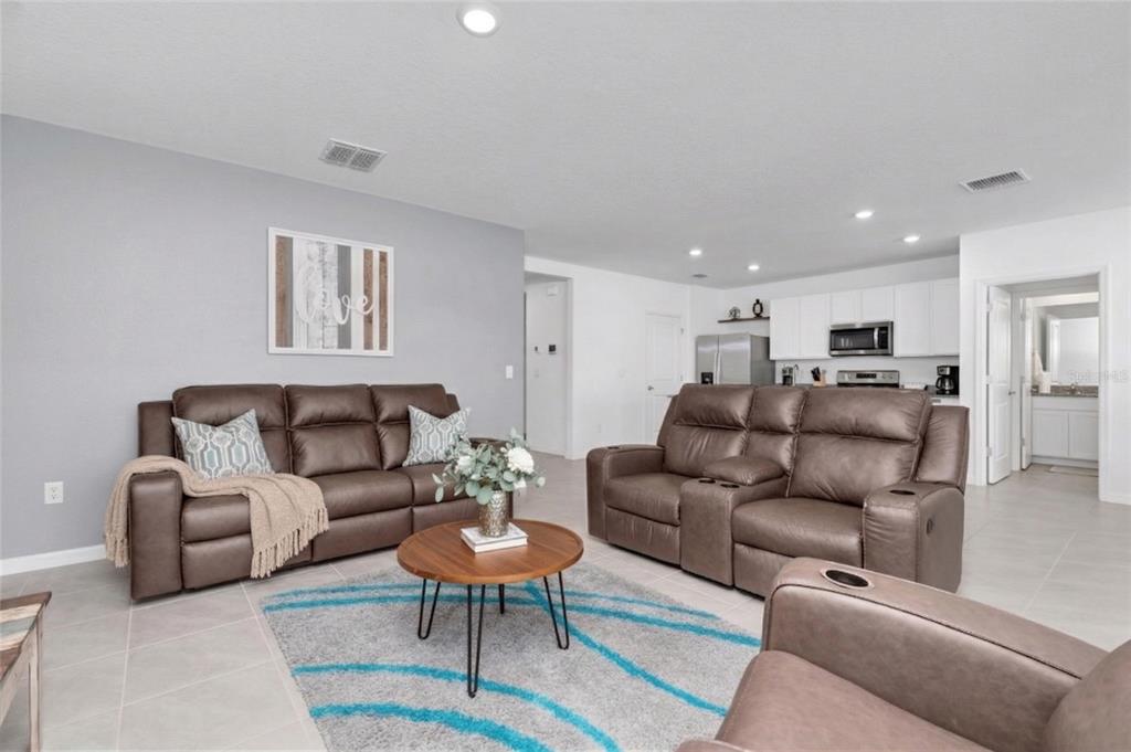 A living room with brown leather reclining sofas, a round coffee table, and an open kitchen — 5943 WANDERING WILLOW DRIVE, WESLEY CHAPEL, FL