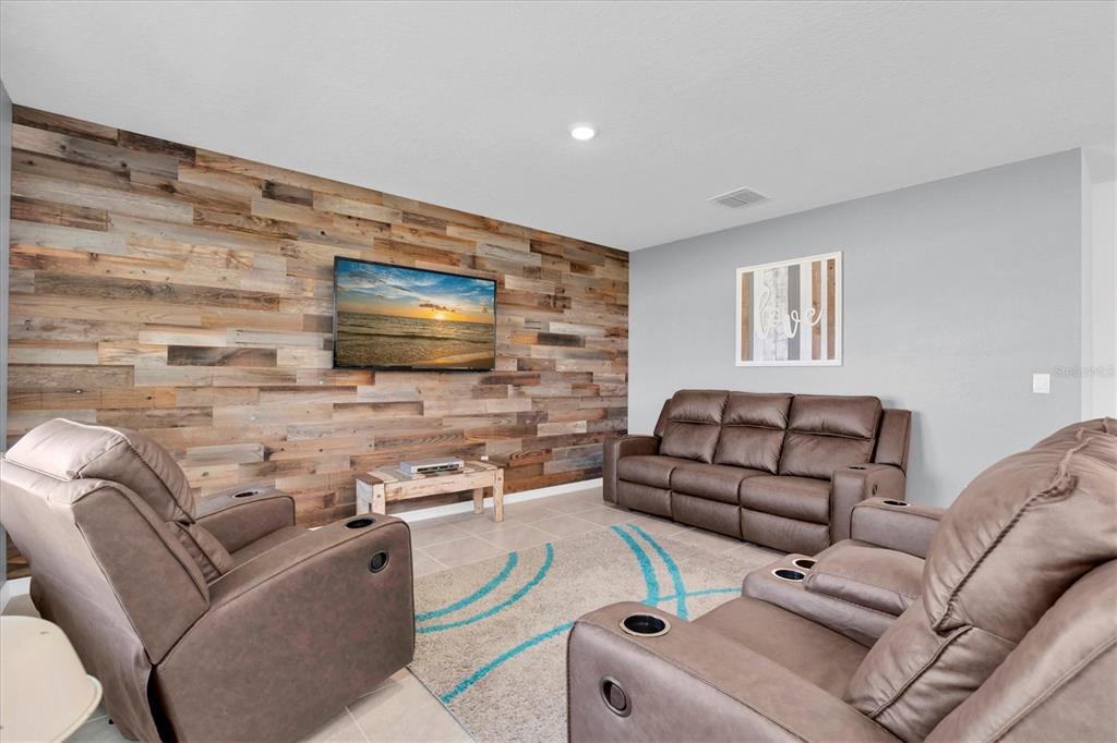 A living room features a wood-plank accent wall, brown leather recliners, and a patterned rug — 5943 WANDERING WILLOW DRIVE, WESLEY CHAPEL, FL