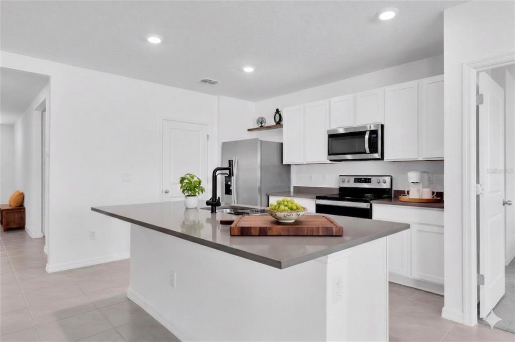 A modern kitchen features white cabinets, stainless steel appliances, and a large gray island — 5943 WANDERING WILLOW DRIVE, WESLEY CHAPEL, FL