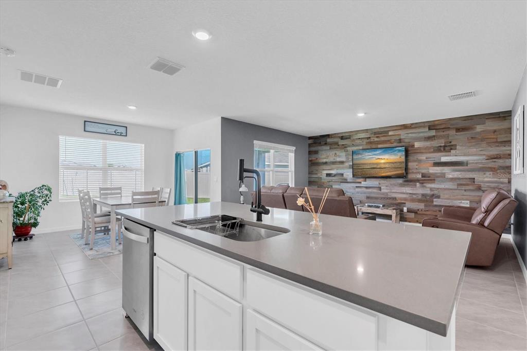 A kitchen island with a sink overlooks an open-concept living room with a wood-paneled wall — 5943 WANDERING WILLOW DRIVE, WESLEY CHAPEL, FL