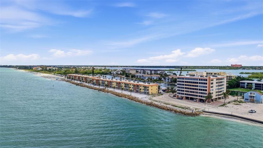 An aerial view shows beachfront apartment buildings along a coastline with a rocky shoreline — 9150 BLIND PASS ROAD UNIT 206, SARASOTA, FL