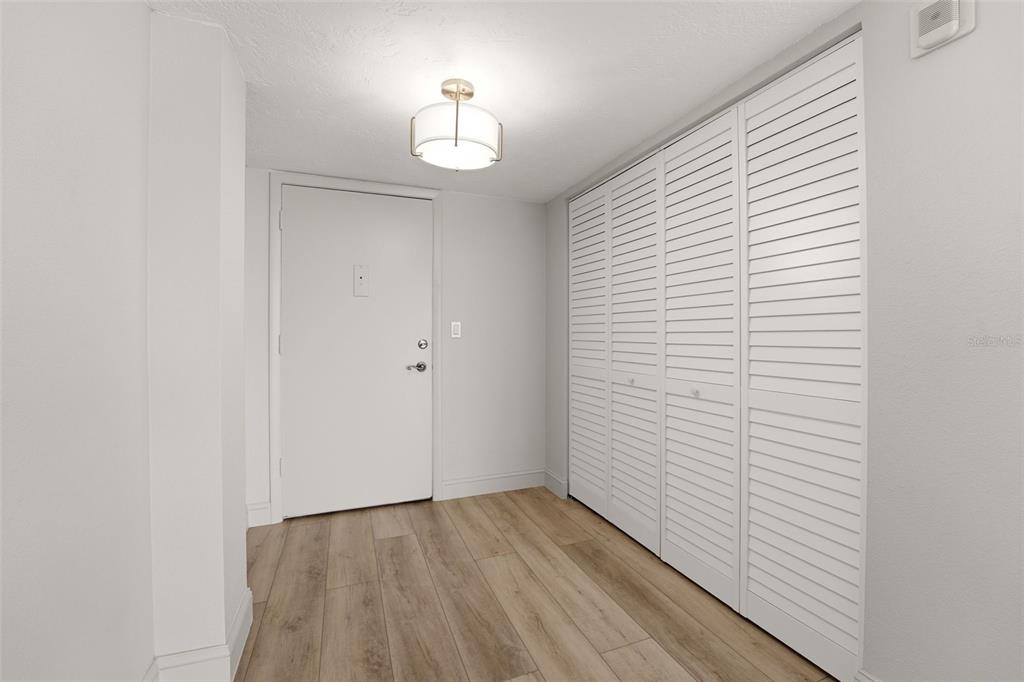 An entryway features light wood-look flooring, a white door, and a large louvered closet — 9150 BLIND PASS ROAD UNIT 206, SARASOTA, FL