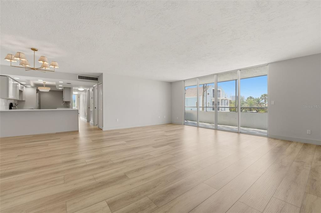 A spacious living room with light wood-look flooring, a kitchen pass-through, and floor-to-ceiling windows — 9150 BLIND PASS ROAD UNIT 206, SARASOTA, FL