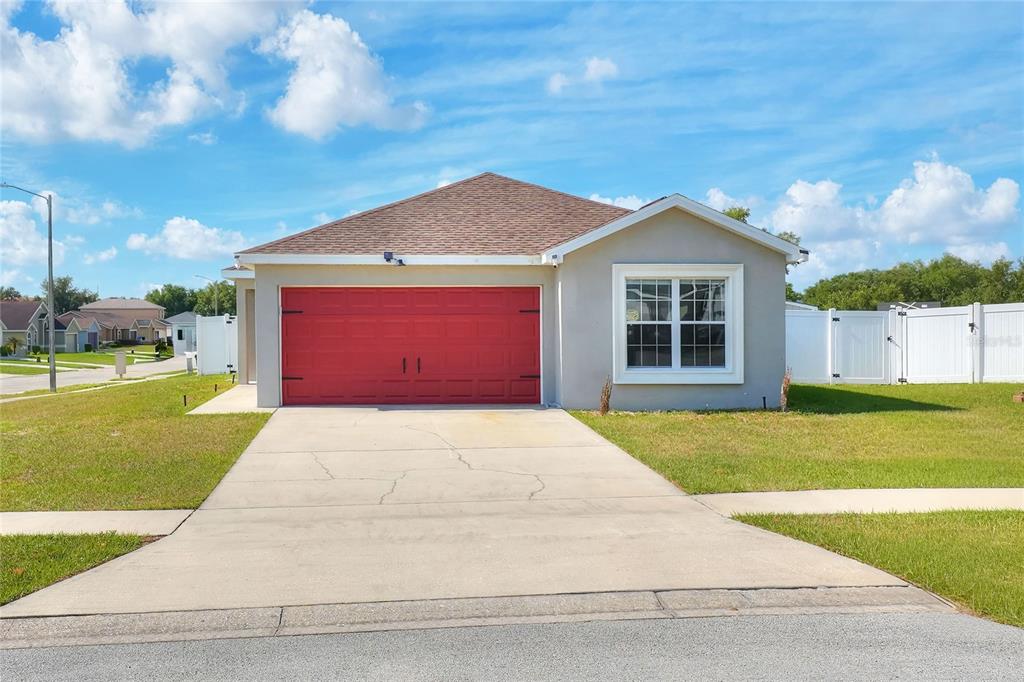 A single-story house features a red garage door, a front window, and a concrete driveway — 780 OVERLOOK GROVE DRIVE, WINTER HAVEN, FL