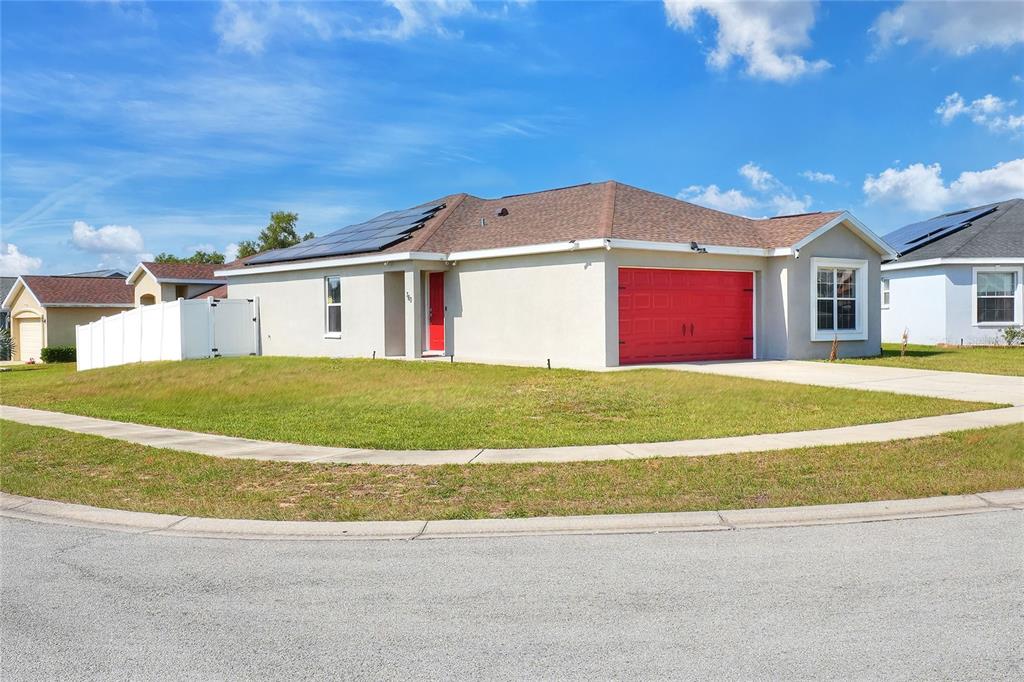 A single-story house with a red garage door, solar panels, and a white fence — 780 OVERLOOK GROVE DRIVE, WINTER HAVEN, FL