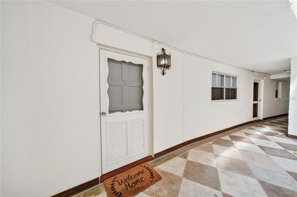 A white door with a screen and a welcome mat sits on a tiled walkway — 601 N MCDONALD STREET UNIT 2, MOUNT DORA, FL