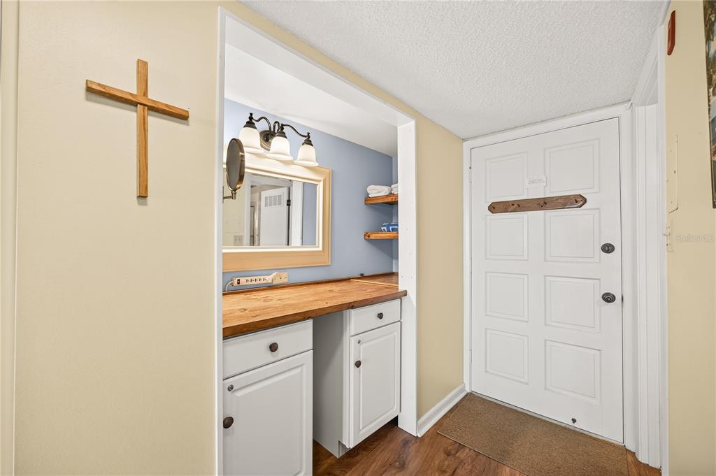 A vanity area with a wooden countertop and mirror sits beside a white entry door — 601 N MCDONALD STREET UNIT 2, MOUNT DORA, FL