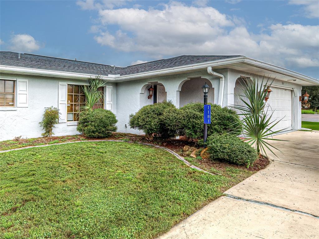 A single-story white house features a covered entryway, a two-car garage, and a front lawn — 1181 SEACREST DRIVE NW, PORT CHARLOTTE, FL