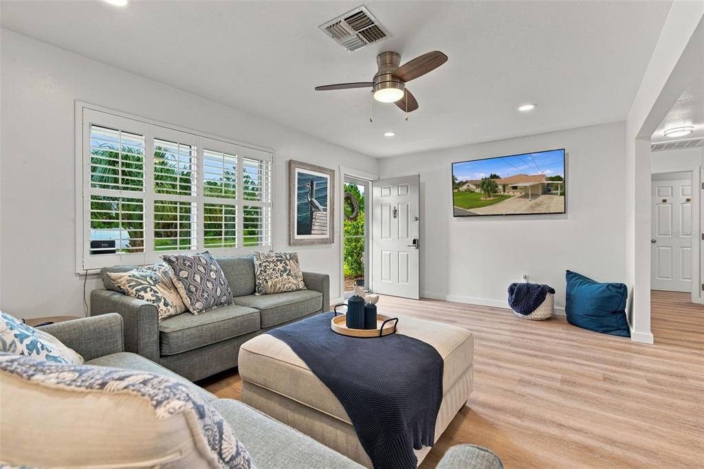 A living room features light wood-look flooring, a gray sofa, an ottoman, and a ceiling fan — 3339 POINSETTIA DRIVE, HERNANDO BEACH, FL