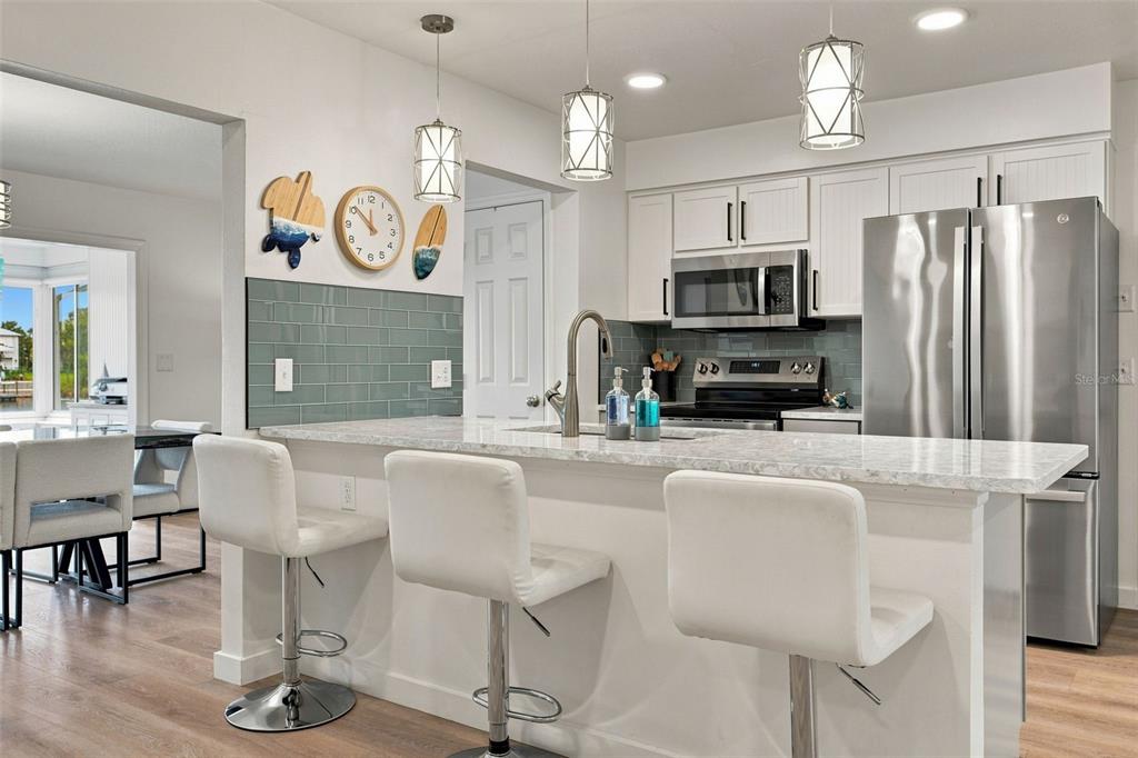 A kitchen features white cabinets, a marble-look island with bar stools, and a teal backsplash — 3339 POINSETTIA DRIVE, HERNANDO BEACH, FL