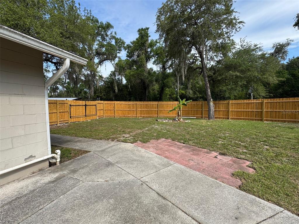 A beige concrete block house features a back patio, a white door, and a yard — 6052 IDLE A WHILE CIRCLE, DADE CITY, FL