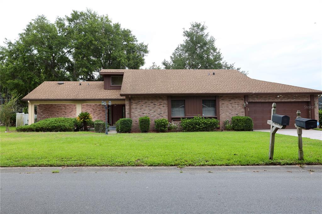 A single-story brick house with a brown shingled roof and an attached two-car garage — 1781 KING CHARLES DRIVE, KISSIMMEE, FL