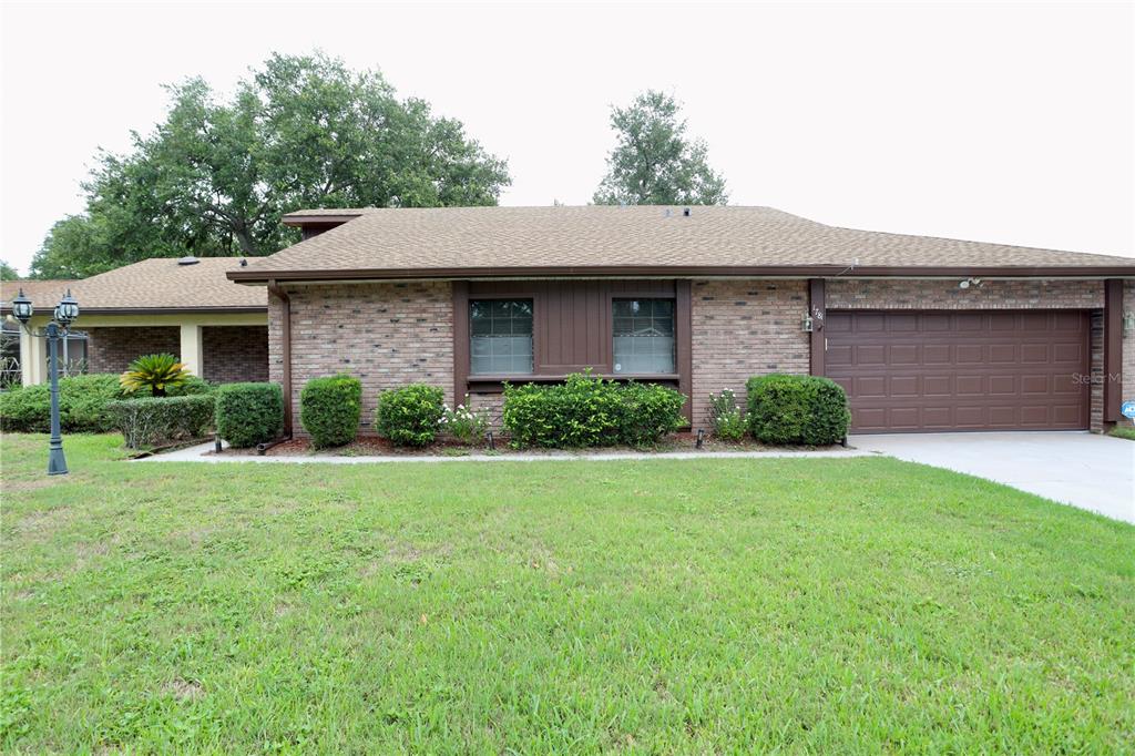 A single-story brick house with a brown shingle roof and an attached two-car garage — 1781 KING CHARLES DRIVE, KISSIMMEE, FL