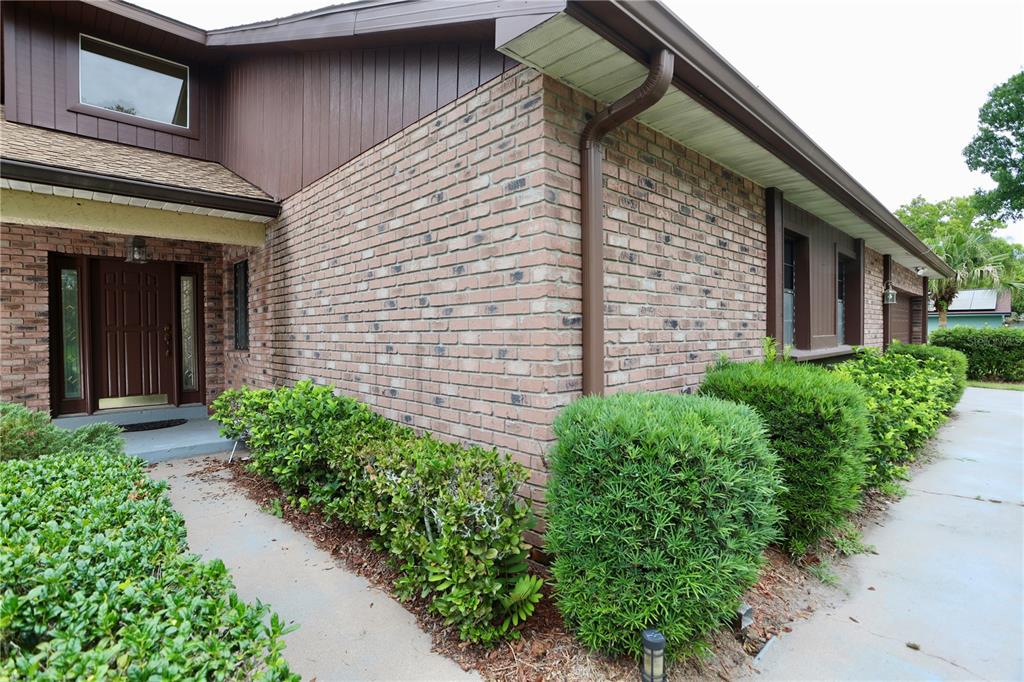A brick exterior house features a brown front door, vertical siding, and manicured green bushes — 1781 KING CHARLES DRIVE, KISSIMMEE, FL