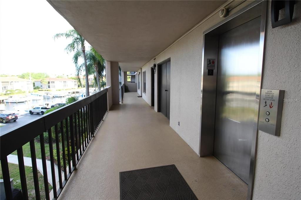 An outdoor apartment hallway features a metal elevator, a dark door, and a balcony railing — 1806 MARINER DRIVE UNIT 214, TARPON SPRINGS, FL