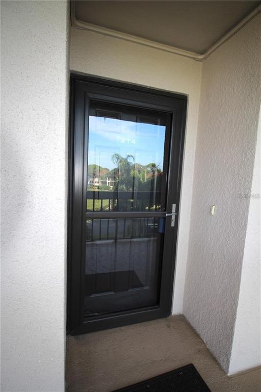 A dark-framed storm door with the number 214 is set into a textured stucco entryway — 1806 MARINER DRIVE UNIT 214, TARPON SPRINGS, FL