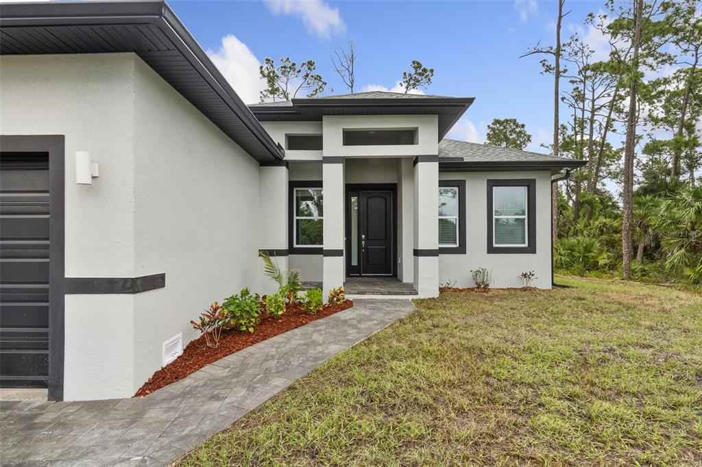 A modern single-story house with a gray exterior, dark trim, and a paved walkway — 18024 PLACID AVENUE, PORT CHARLOTTE, FL