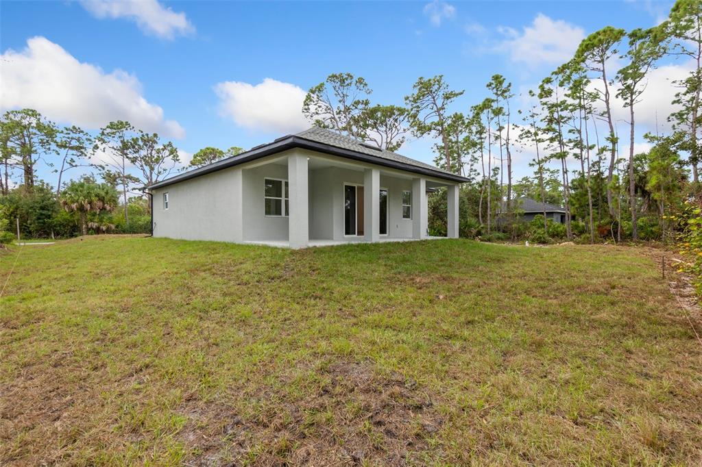 The exterior of a light-colored, single-story house features a covered patio and surrounding yard — 18024 PLACID AVENUE, PORT CHARLOTTE, FL