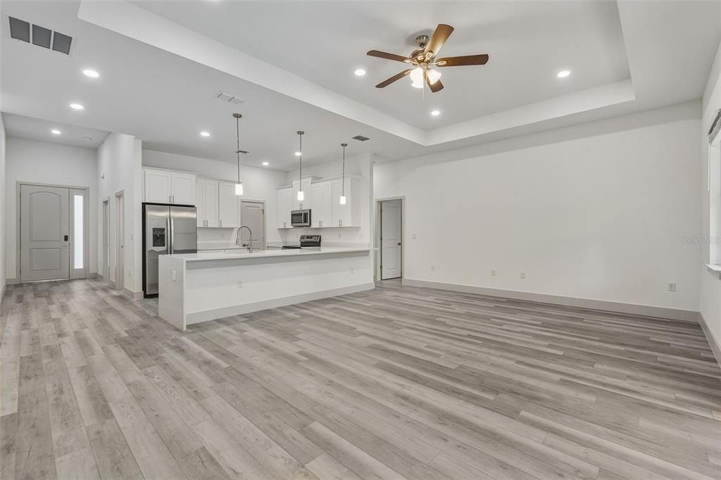 An open-concept kitchen and living area feature light wood-look flooring and a tray ceiling — 18024 PLACID AVENUE, PORT CHARLOTTE, FL