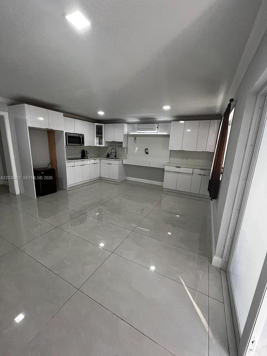 A modern kitchen features white cabinetry, glossy tile flooring, and a built-in microwave — 1271 W 79th St, Hialeah FL 33014, HIALEAH, FL