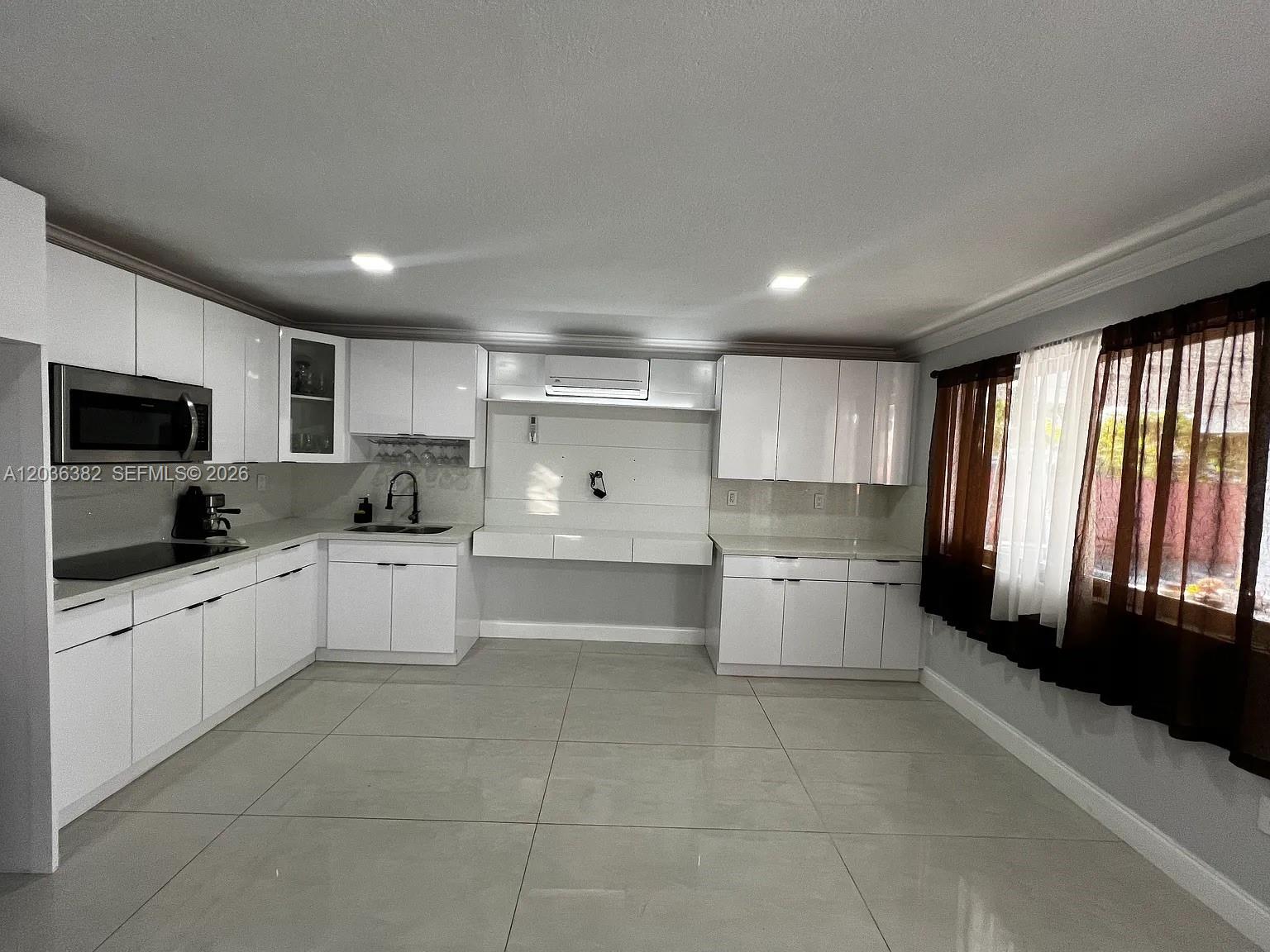 A modern kitchen features white glossy cabinets, stainless steel appliances, and large light-colored floor tiles — 1271 W 79th St, Hialeah FL 33014, HIALEAH, FL