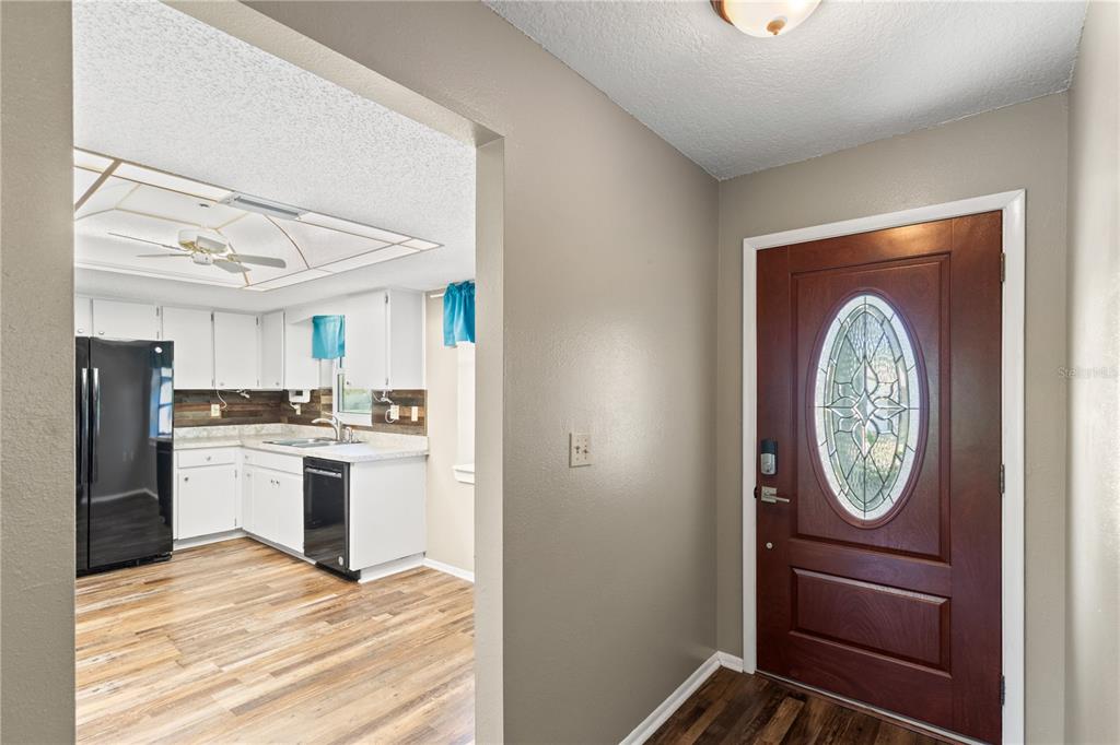 An entryway with a wood-paneled front door leads into a kitchen with white cabinets — 10616 SPRINGWOOD DRIVE, PORT RICHEY, FL