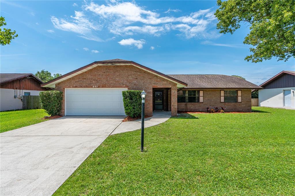A single-story brick house with a two-car garage and a front lawn under blue skies — 897 WHIPORWILL DRIVE, PORT ORANGE, FL
