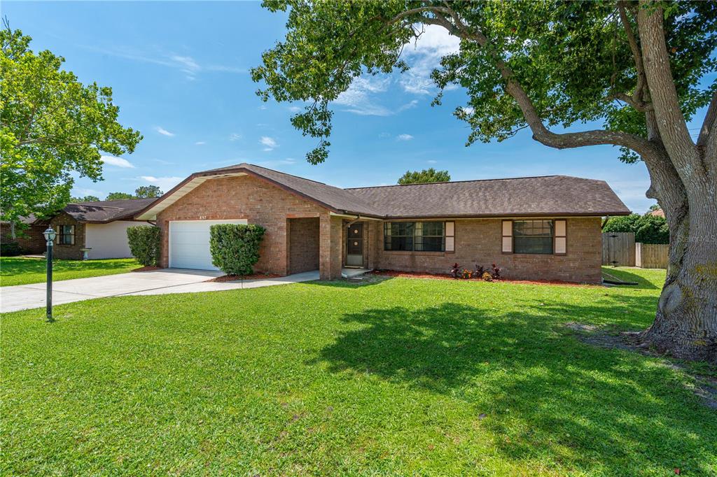 A single-story brick house with a front-facing garage and a large tree in the yard — 897 WHIPORWILL DRIVE, PORT ORANGE, FL
