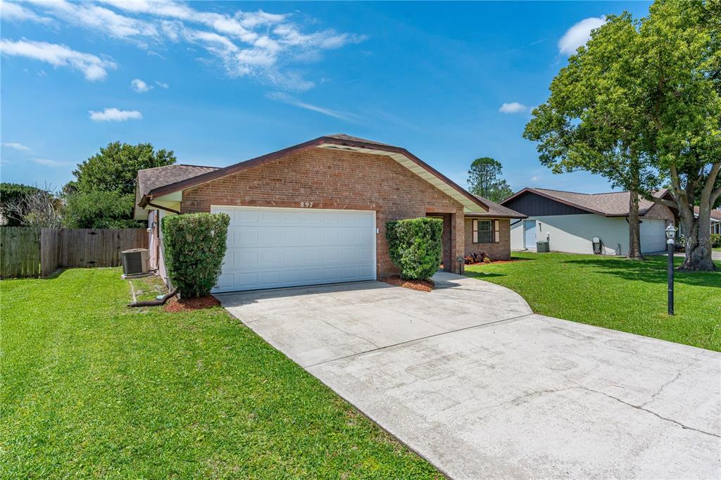 A single-story brick house features a two-car garage, a concrete driveway, and a grassy lawn — 897 WHIPORWILL DRIVE, PORT ORANGE, FL