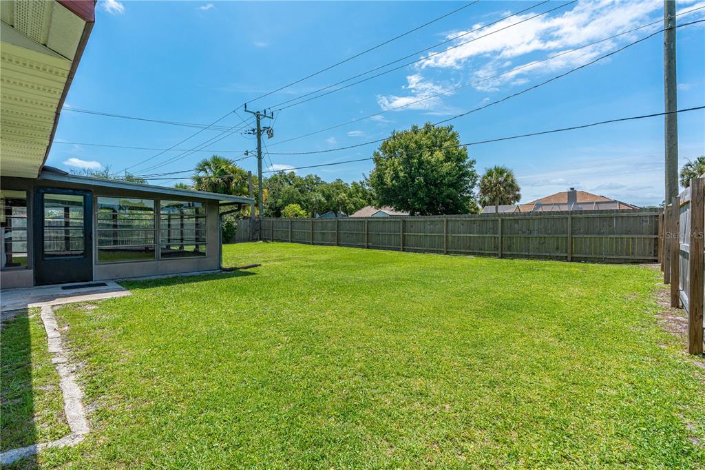 A grassy backyard features a fenced perimeter, a screened-in patio, and overhead utility lines — 897 WHIPORWILL DRIVE, PORT ORANGE, FL