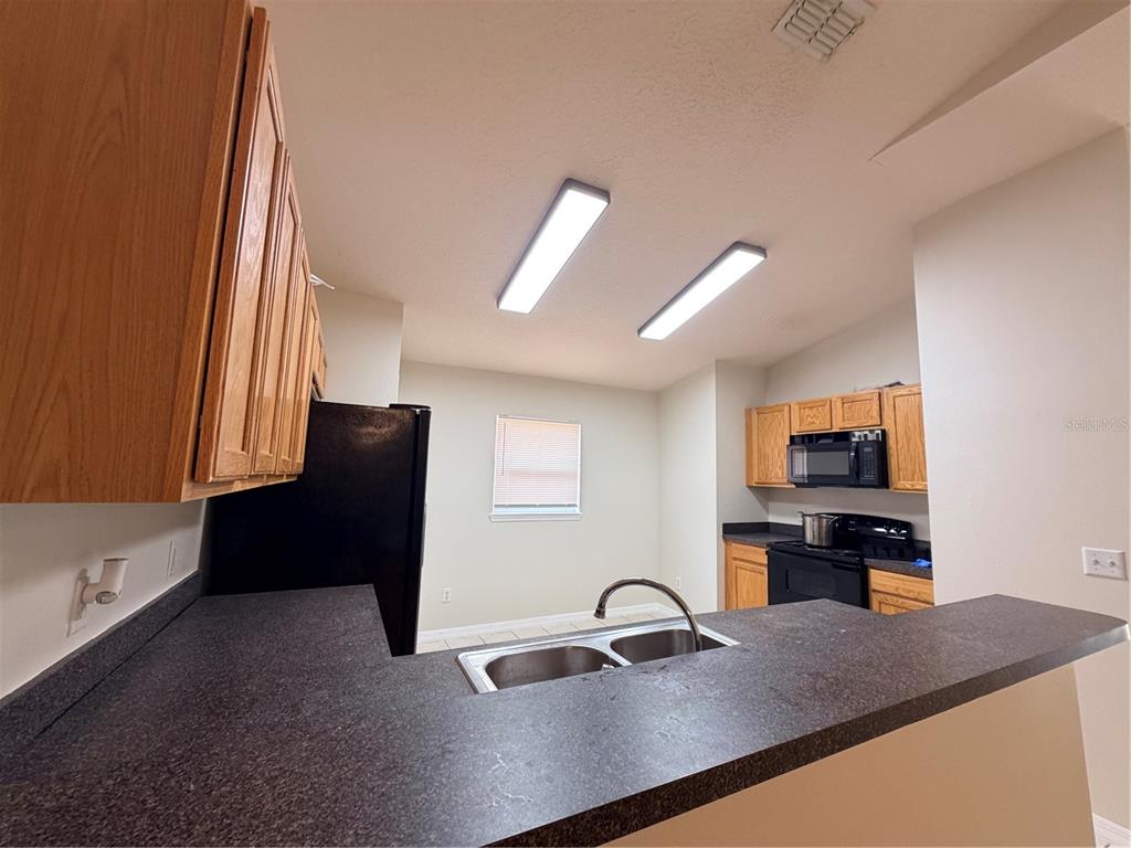 A kitchen with wooden cabinets, black appliances, a double sink, and dark countertops — 175 RIDGEBROOK COURT, DAVENPORT, FL