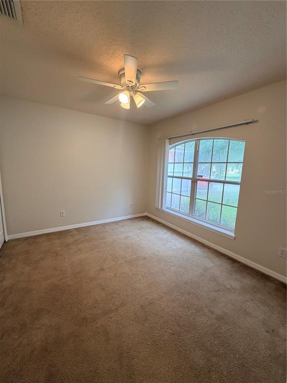 An empty bedroom features beige carpet, light-colored walls, a ceiling fan, and a large window — 175 RIDGEBROOK COURT, DAVENPORT, FL