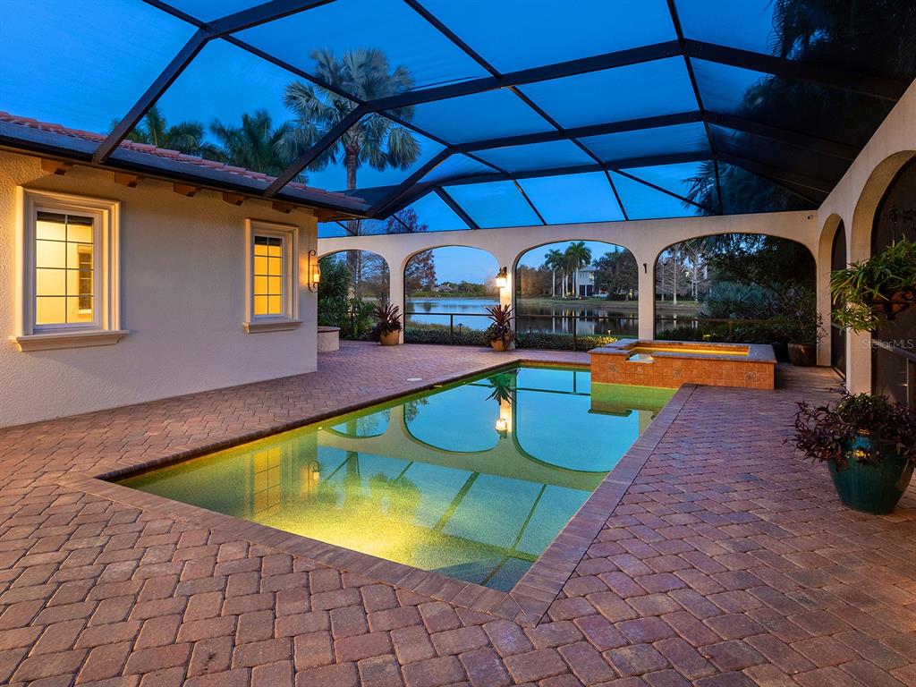 A screened-in patio features a swimming pool, a raised spa, and brick pavers at dusk — 7951 MATERA COURT, LAKEWOOD RANCH, FL