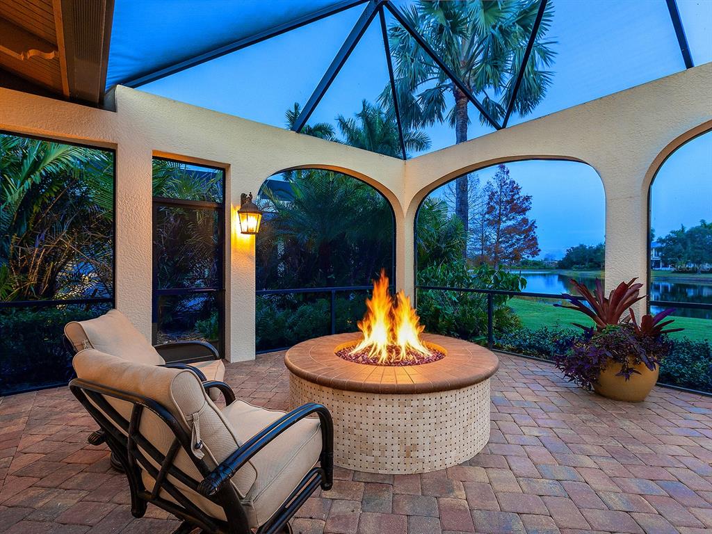 A screened-in patio features a circular stone fire pit, outdoor seating, and a lake view — 7951 MATERA COURT, LAKEWOOD RANCH, FL