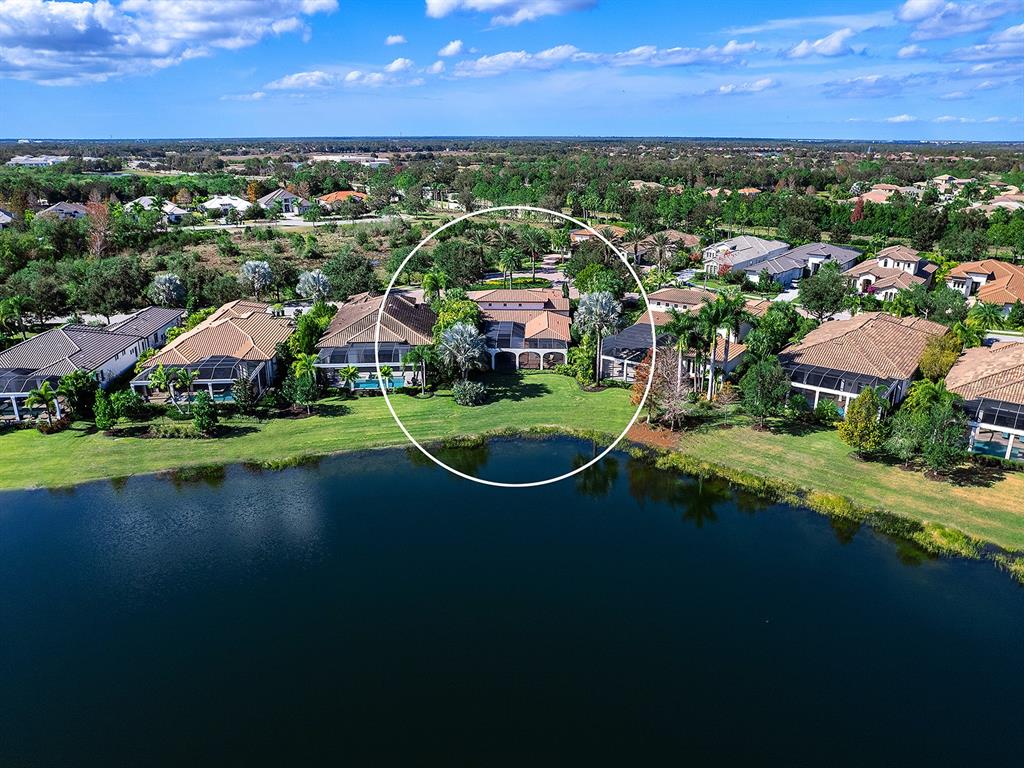 An aerial view shows a residential house with a pool enclosure overlooking a lake — 7951 MATERA COURT, LAKEWOOD RANCH, FL