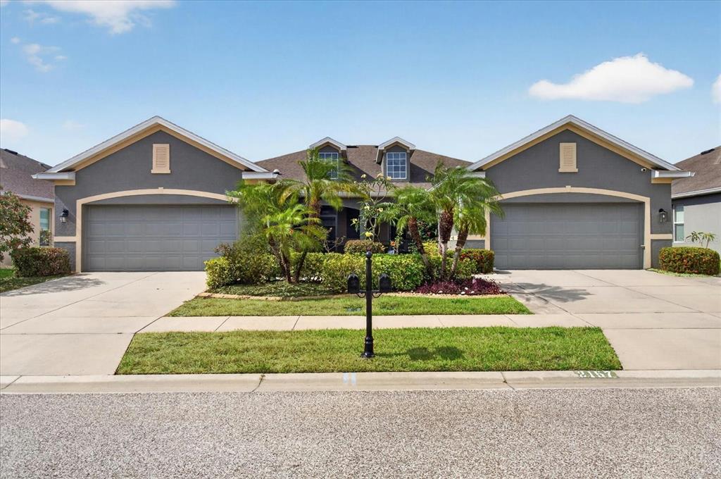 A gray duplex house features two garage doors, a central entrance, and palm trees — 2153 BARRACUDA COURT, HOLIDAY, FL