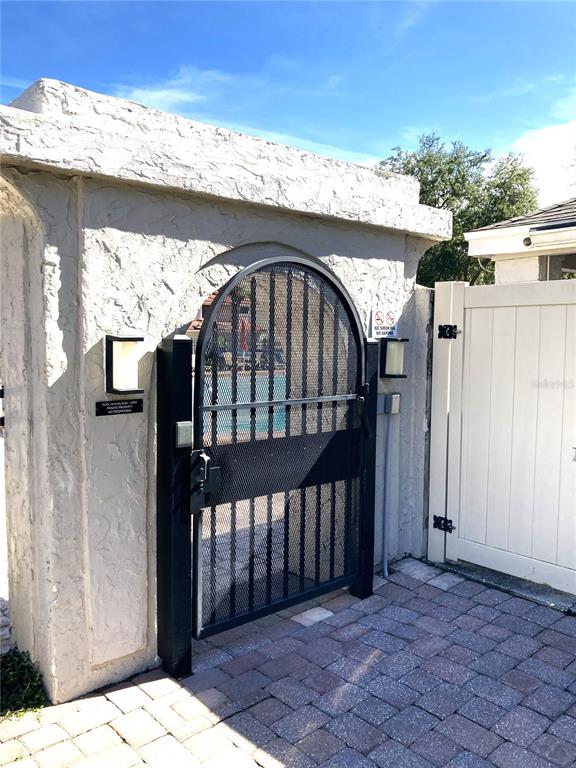 A black metal arched gate is set into a textured stucco wall with outdoor lighting — 8214 AMBROSE COVE WAY, ORLANDO, FL