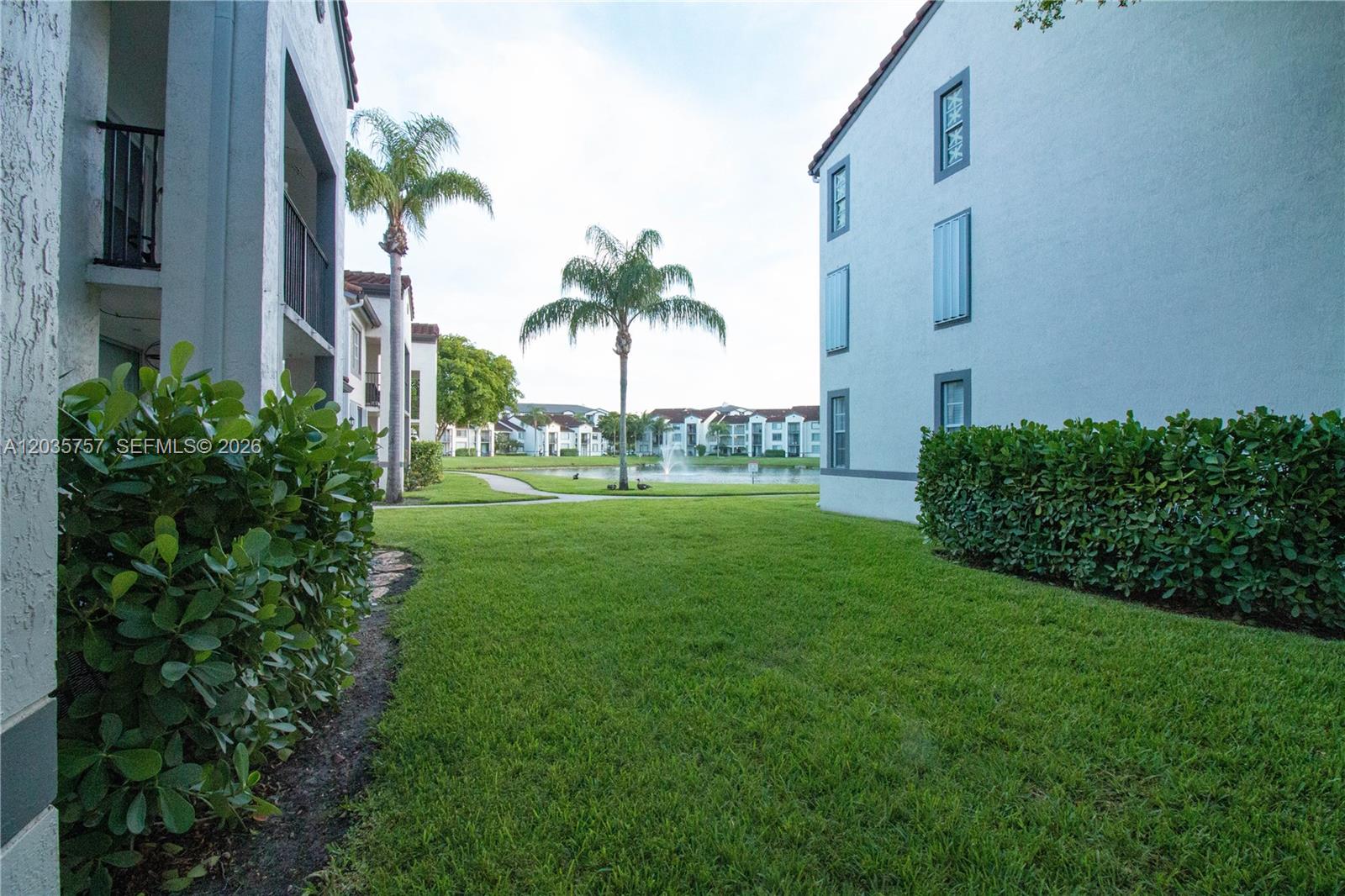 A grassy courtyard sits between two apartment buildings with a small pond and palm trees — 4500 NW 107th Ave # 9, Doral FL 33178, DORAL, FL
