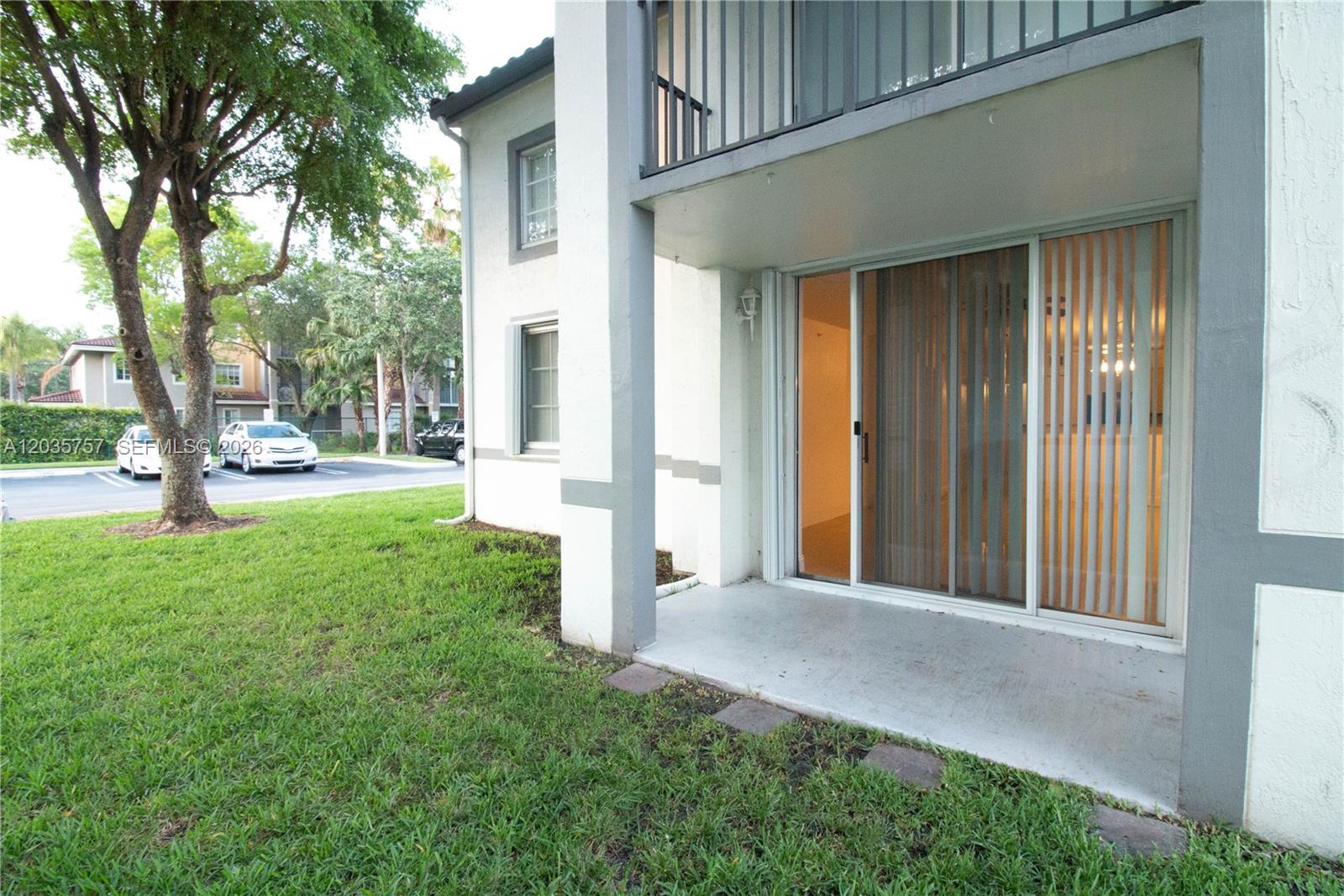 A ground-floor patio with sliding glass doors sits beside a grassy lawn and large tree — 4500 NW 107th Ave # 9, Doral FL 33178, DORAL, FL